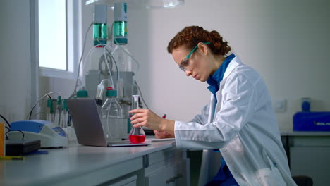 Scientist-find-a-cure.-Woman-scientist-looking-at-chemical-liquid-in-lab-flask
